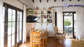 Una stanza con una grande finestra, una televisione, una libreria, un tavolo da pranzo con sedie e una pianta.