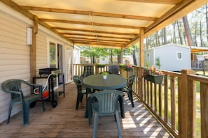 Un espace extérieur abrité, équipé d’une table et de chaises, d’un barbecue et d’une terrasse en bois.
