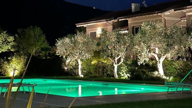 Vista nocturna de un edificio con piscina, rodeado de árboles y una montaña al fondo.