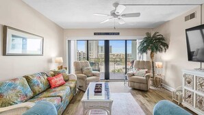 Ein Wohnzimmer mit einer Couch, Sesseln, einem Couchtisch, einem Fernseher und einem Balkon mit Blick auf die Stadt.