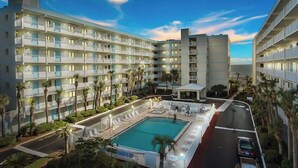 Ein mehrstöckiges Hotel mit Balkonen, einem Swimmingpool und Palmen.
