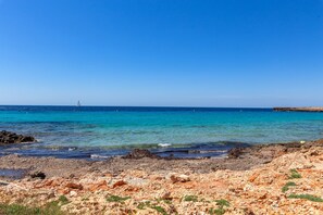 Ein felsiger Strand mit klarem, blauem Wasser und einem entfernten Segelboot.