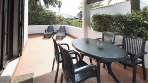 Um pátio externo com uma mesa redonda e seis cadeiras, cercado por um muro branco e vegetação.