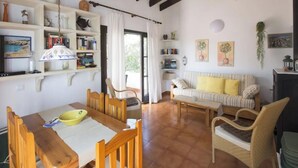 Uma sala de estar acolhedora com uma mesa de jantar, cadeiras, um sofá e uma estante de livros.