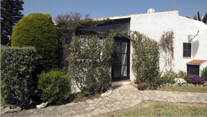 Um edifício branco com porta preta, cercado por vegetação e um caminho de pedra.