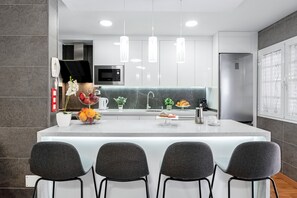 A modern kitchen with a central island, bar stools, a microwave, and pendant lights.