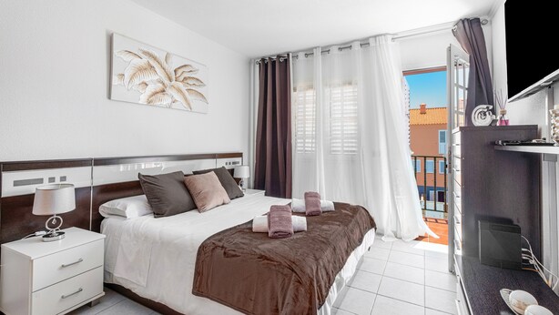 A hotel room with a bed, a nightstand, a window with curtains, and a view of buildings outside.