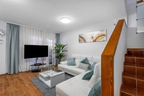Un salon moderne avec un téléviseur à écran plat, un canapé blanc et un escalier.