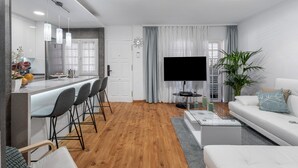 A modern living room with a white sofa, a TV, and a dining area with bar stools.