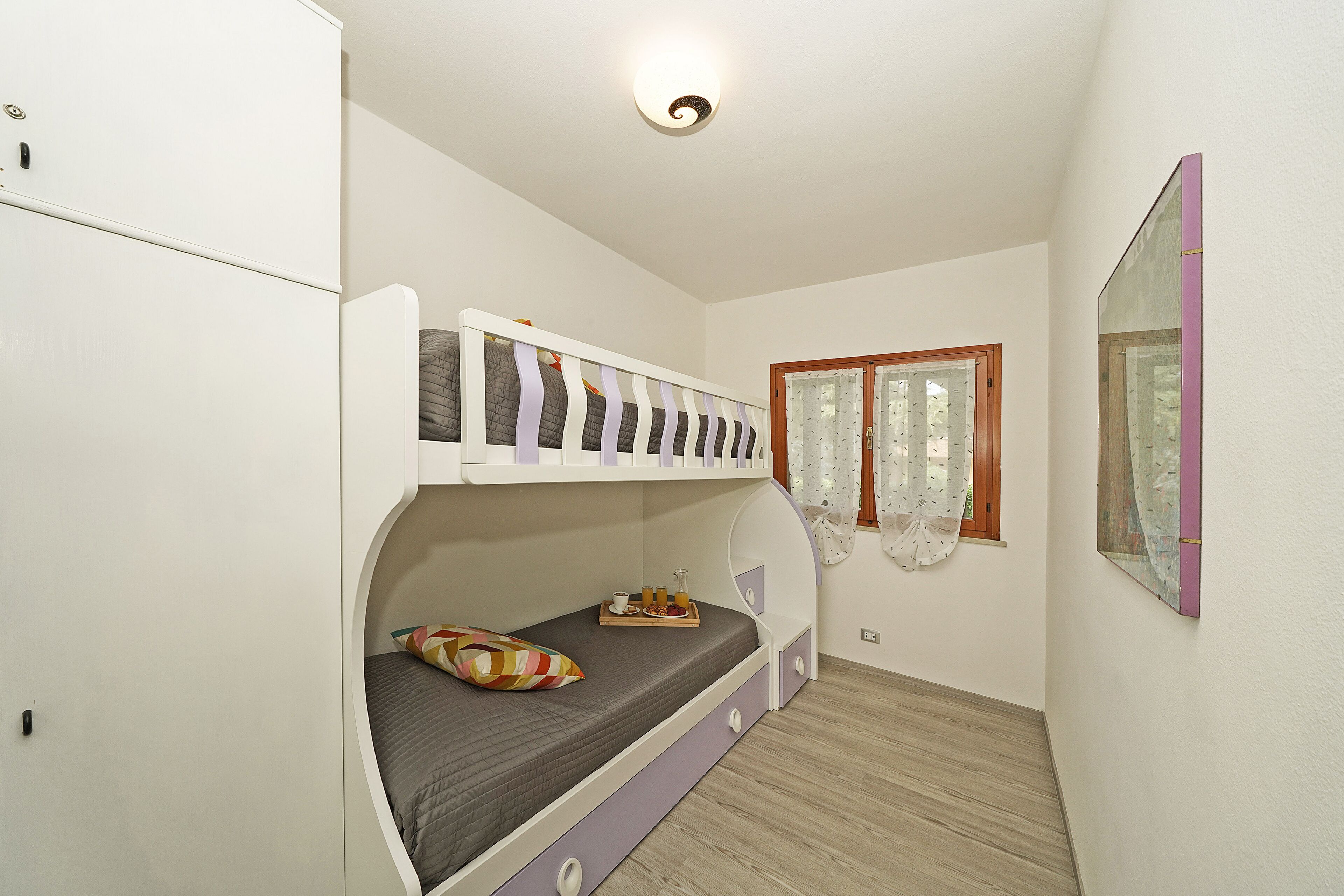 Un lit superposé avec un plateau de collations, une fenêtre avec des rideaux et un miroir sur le mur.