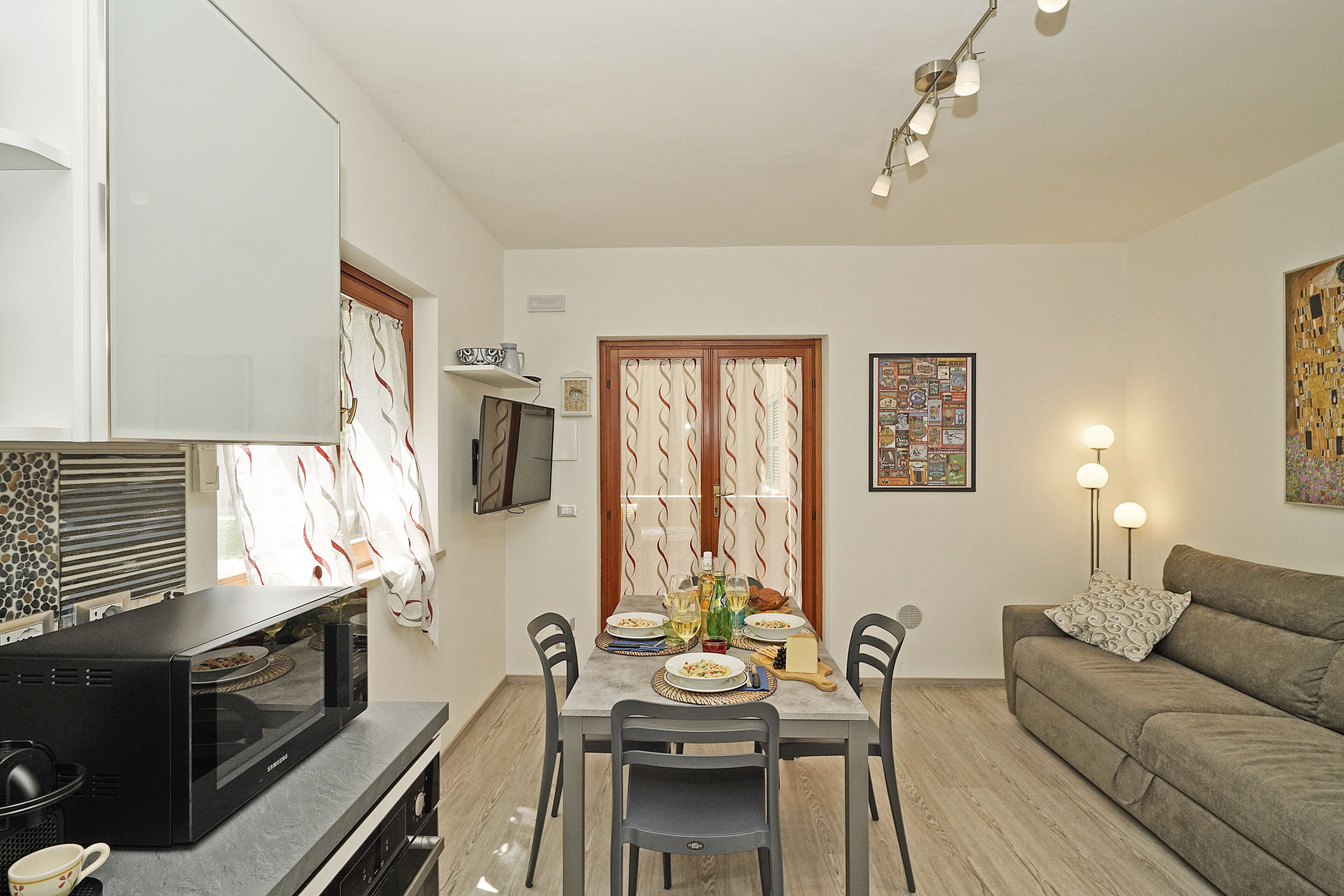 Un comedor con una mesa preparada para cuatro personas, un sofá, un televisor y una cocina con microondas.