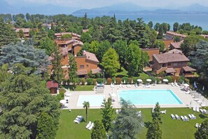 A resort with a large swimming pool, multiple lounge areas, and a view of the sea. - Residence Punta Gro by Wonderful Italy (Sirmione)