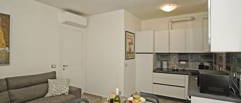 Un espacio habitable compacto con comedor, kitchenette y un sofá gris.