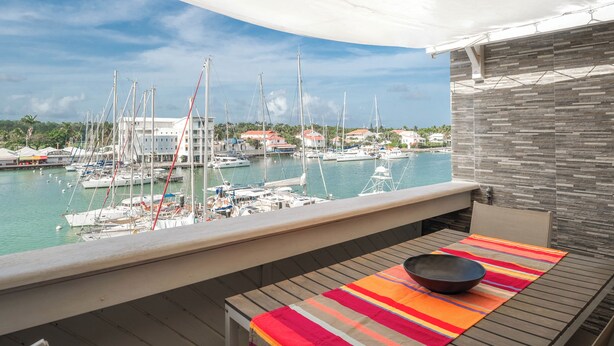 A balcony with a view of a marina, a table with a colorful table runner, and a chair. - Honoré apartment with views of the marina and golf course 2mn from beaches (Saint-François)