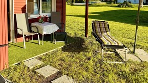 A red building with a covered patio, a table with chairs, and a lounge chair. - Cozy I Log cabin in the Bavarian Forest I National Park (Neureichenau)