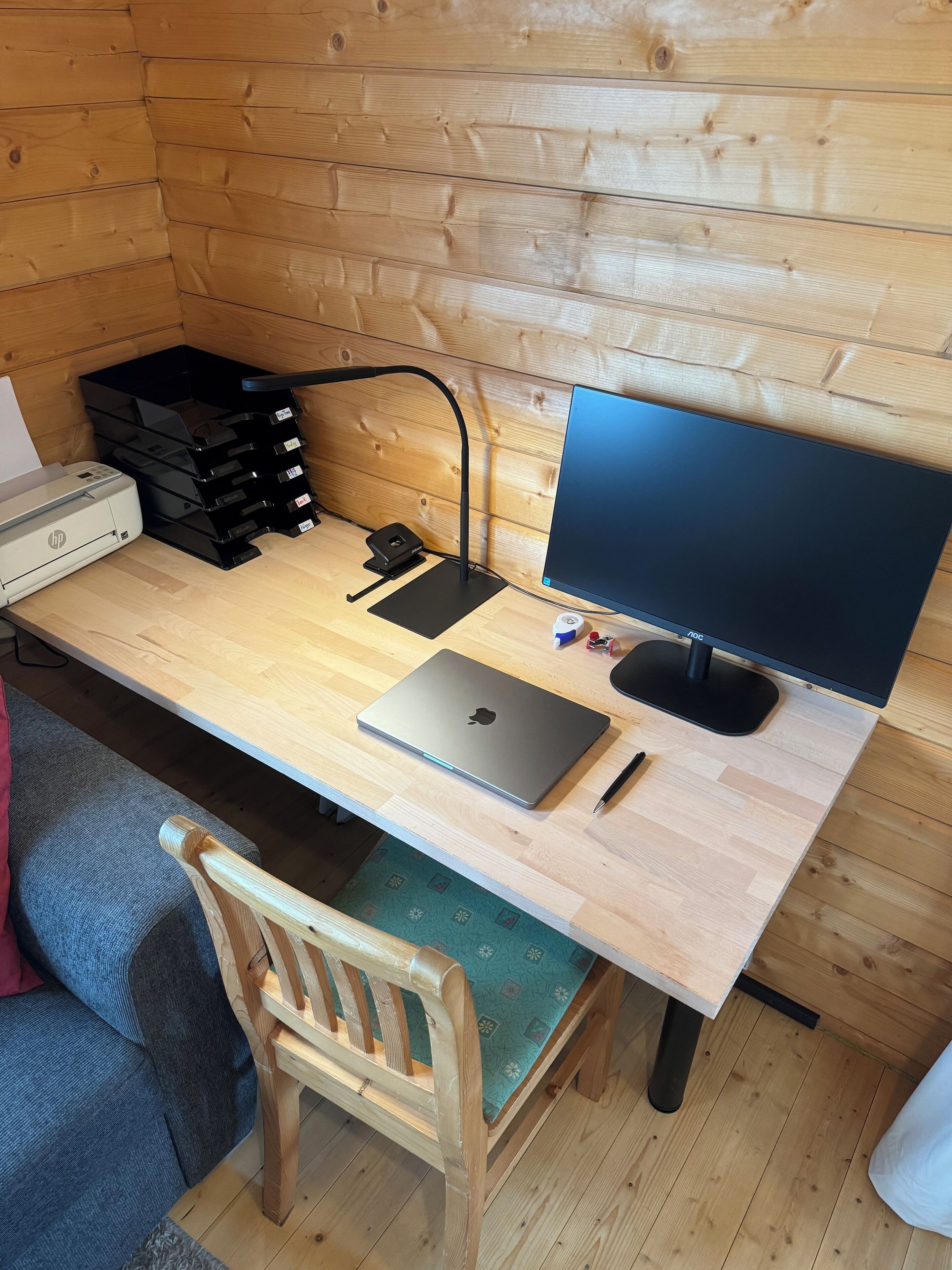 Interior de una cabaña de madera con un escritorio, laptop, impresora y contenedores de almacenamiento.