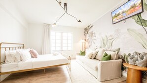Ein Schlafzimmer mit einem Bett, einer Couch, einem Fernseher und einer Pflanze.