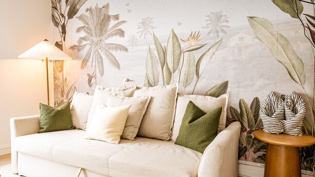 Ein Wohnzimmer mit einer Couch, Kissen, einer Lampe und einer Wandmalerei.