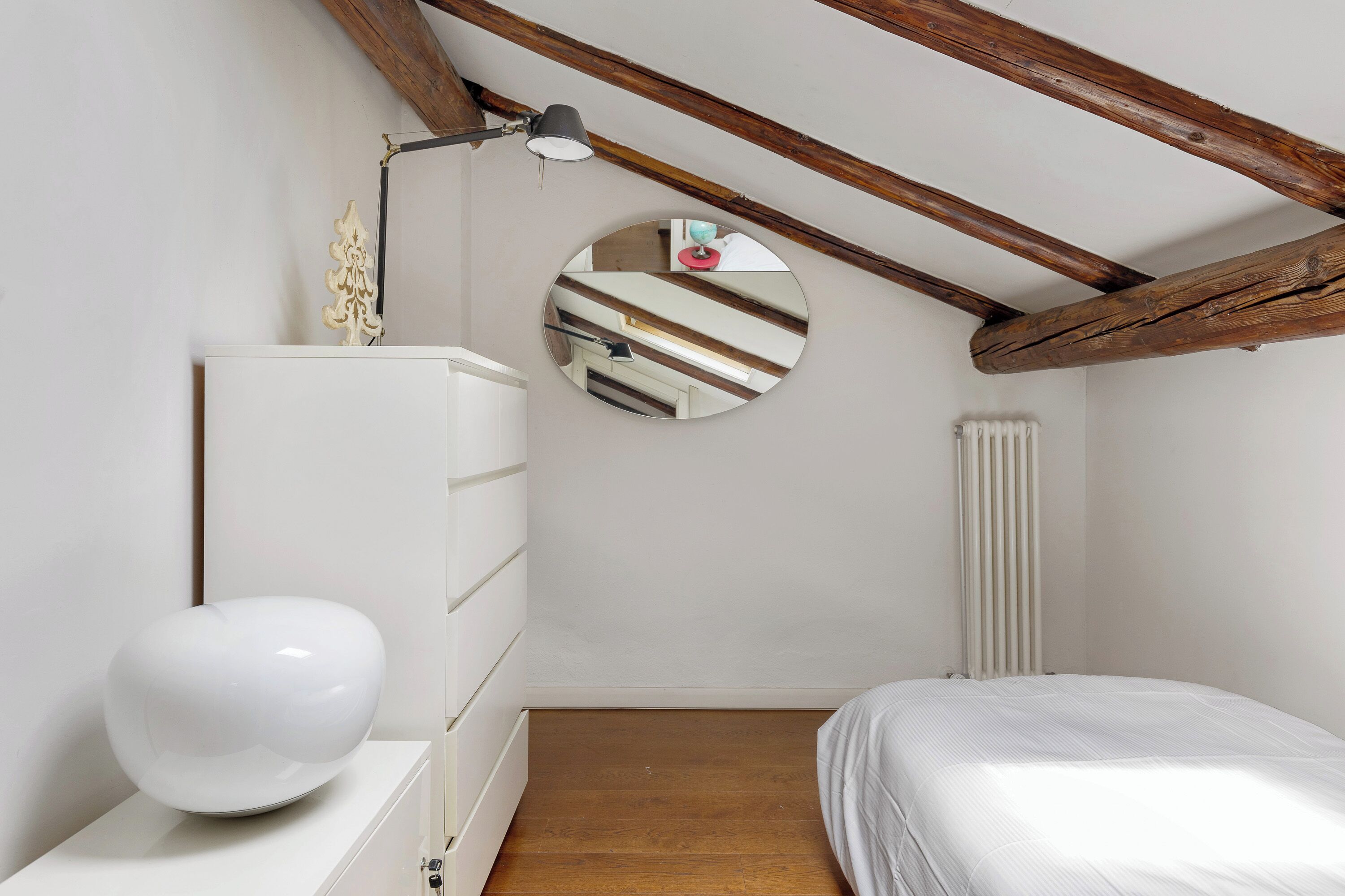 Un dormitorio con techo de madera, un espejo redondo, un aparador blanco y una cama.