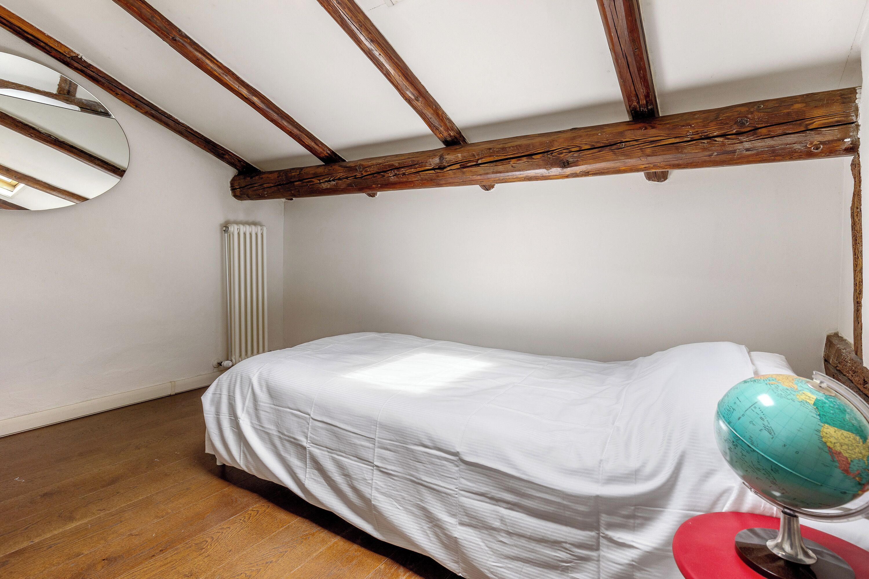 A bedroom with a single bed, a globe on a red stand, and a radiator on the wall.