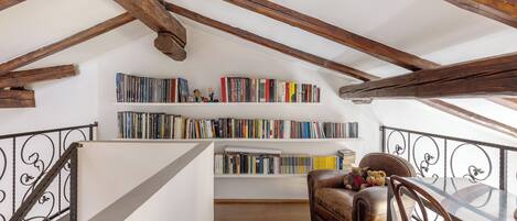 Un espacio tipo loft con vigas de madera a la vista, una estantería llena de libros, un sofá de cuero y una mesa de comedor.