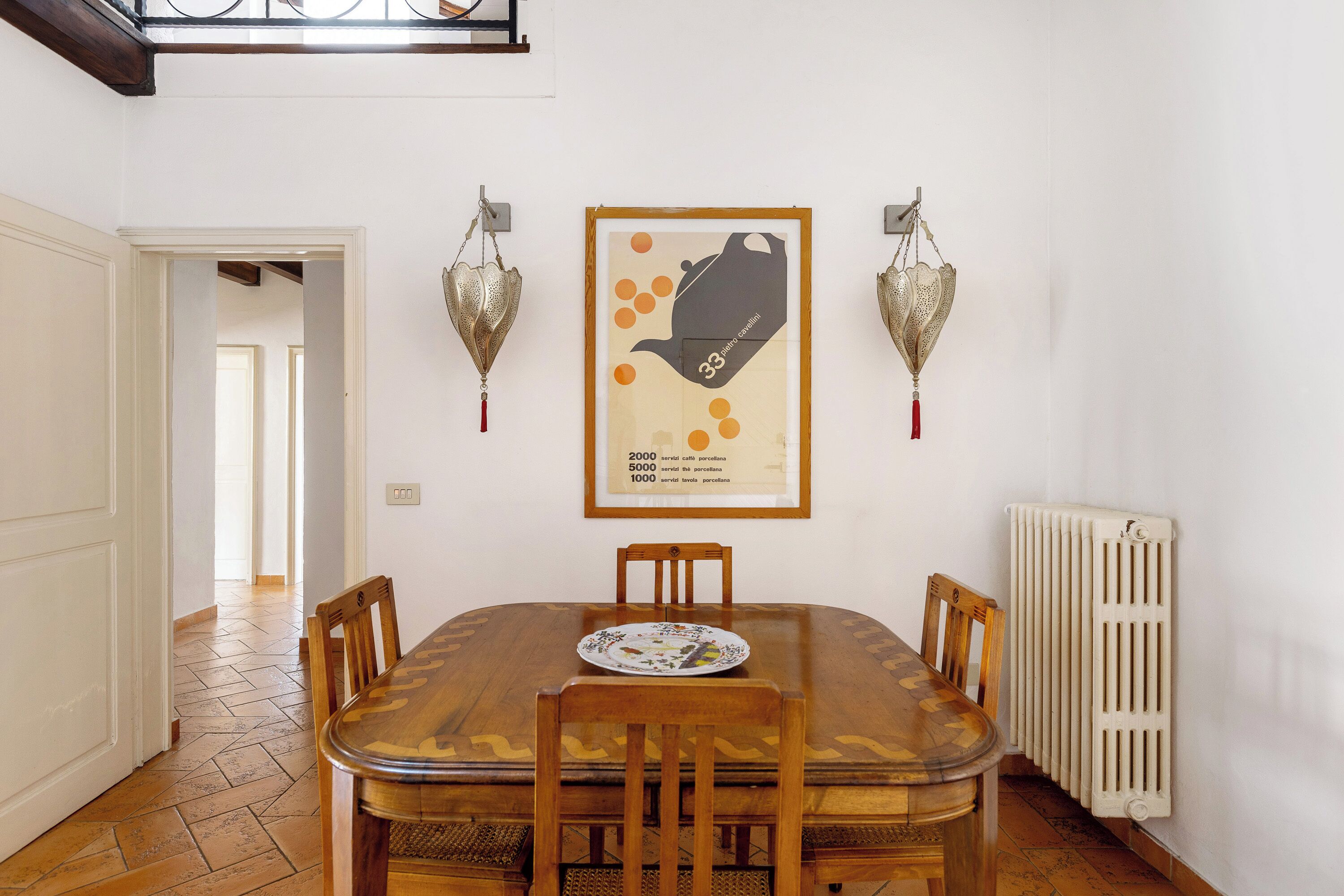 A dining area with a wooden table and chairs, a framed poster on the wall, and a radiator.