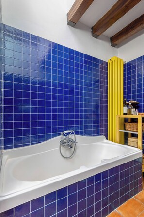 A bathroom with a bathtub, blue tiles, a yellow towel rack, and a wooden ceiling beam. - Country Style House in Bologna by Wonderful Italy (Bologna)