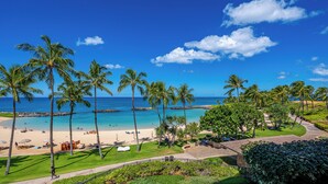 Un complexe hôtelier de style tropical situé sur une plage, avec des palmiers, un ciel bleu azur et une vue sur l’océan.