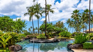 Un complexe hôtelier tropical doté d’une piscine entourée de palmiers et d’une végétation luxuriante.