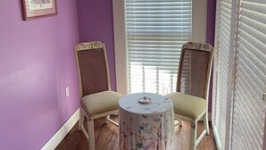 A room with purple walls, a window with blinds, two wicker chairs, and a small round table with a floral tablecloth. - Irishette (Dublin)