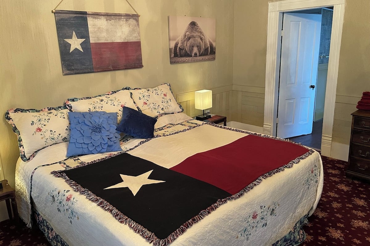 A bed with a Texas flag, floral pillows, and a star-patterned quilt.