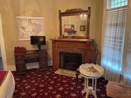 A room with a fireplace, a desk with a computer, a map on the wall, and a window with blinds.