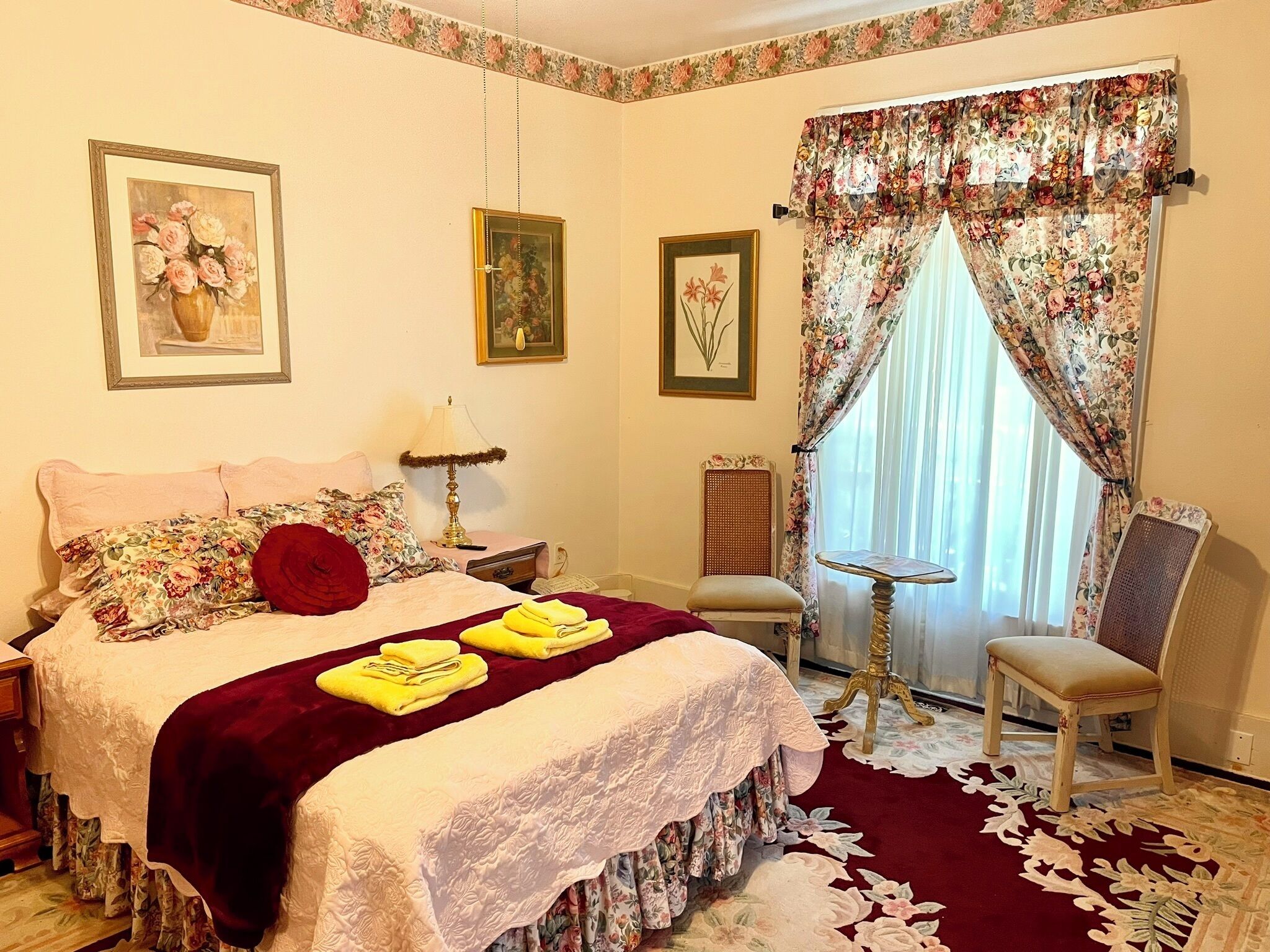 A bedroom with a bed, a chair, a small table, and a window with floral curtains.