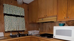 Una cucina compatta con mobili in legno, un forno a microonde, un fornello e una finestra con tende decorate.
