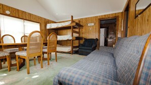 Una stanza con un letto a castello, un divano, un tavolo da pranzo con sedie e un angolo cottura.