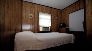 Un letto singolo in una stanza con rivestimenti in legno, una finestra con persiane, un televisore e una porta.