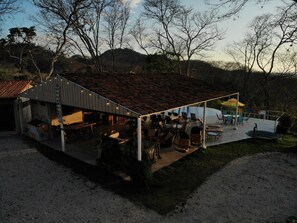 A covered outdoor area with tables and chairs, a pool, and a building with a tiled roof. - Guanaglamp (Tamarindo)