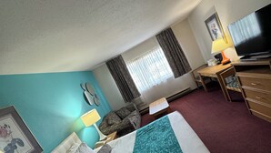Habitación de hotel con cama, escritorio, televisor y ventana con cortinas.