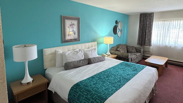 Habitación de hotel con cama, mesita de noche, lámpara, silla y ventana con cortinas.