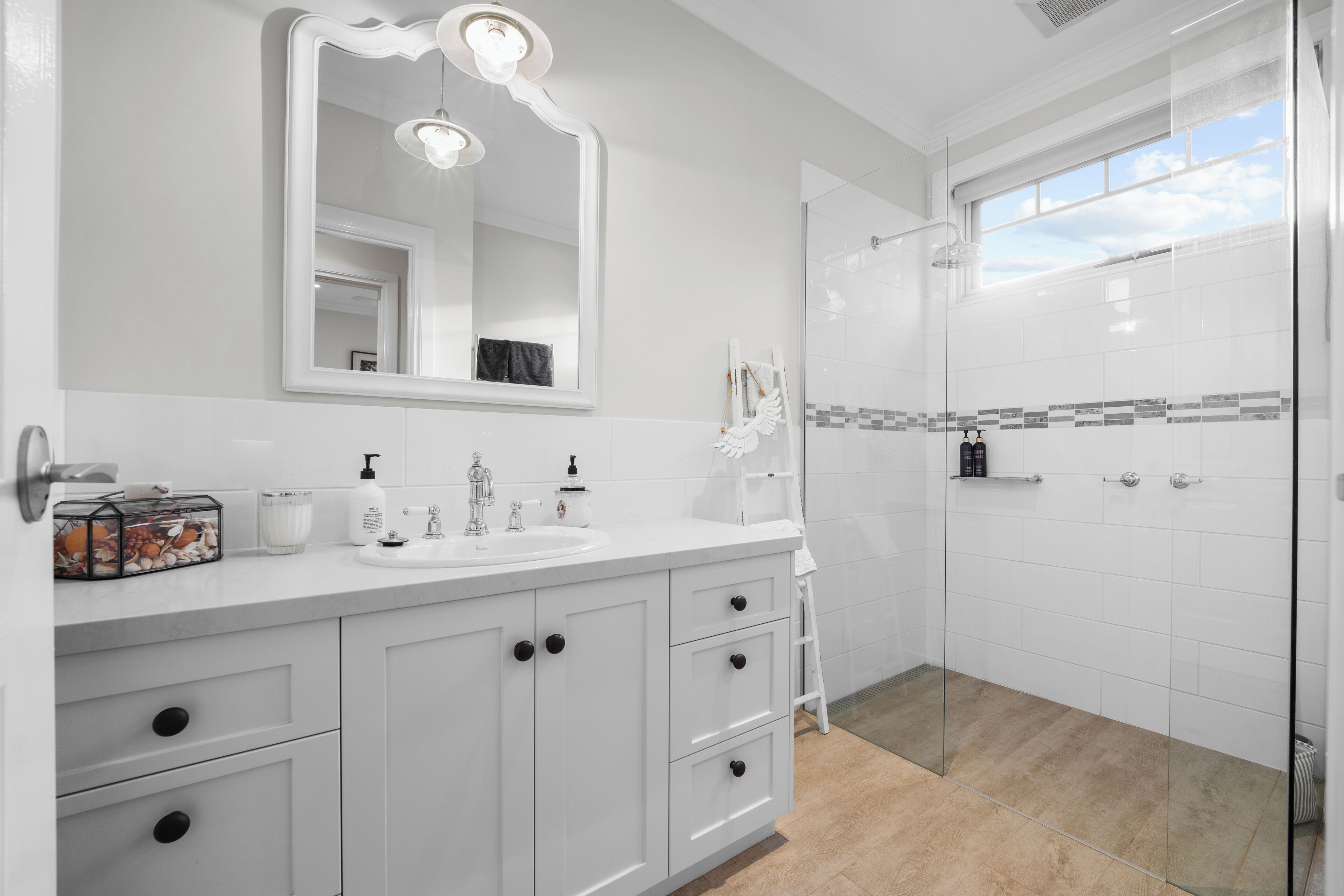 A modern bathroom with a large mirror, white cabinets, a glass shower enclosure, and a tiled shower area.