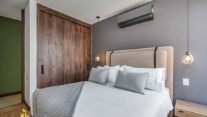 Un dormitorio con cama, mesitas de noche, un armario de madera y un aire acondicionado instalado en la pared.