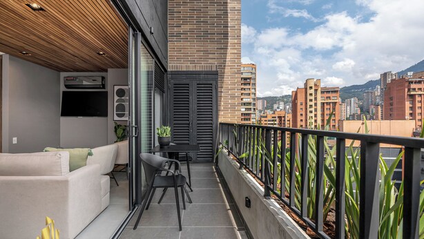 Un balcón con sofá, mesa y sillas. Hay una planta en maceta y una barandilla negra.