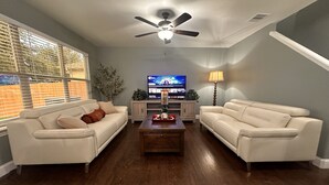 Ein Wohnzimmer mit zwei weißen Ledersofas, einem Holztisch, einem Deckenventilator, einem Fernseher und einer Lampe.