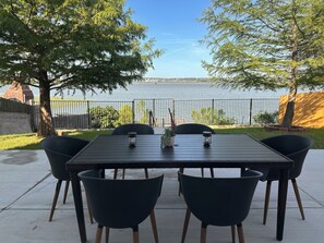 A wooden table with four chairs, a potted plant, and two lanterns on a patio overlooking a body of water. - Cozy Lakefront Home with Private Dock, Grill, & Stunning Views– Near AT&T  (Grand Prairie)