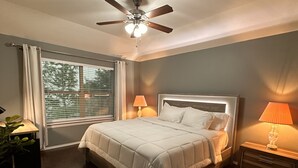 Ein Schlafzimmer mit einem Bett, einem Deckenventilator, einem Fenster mit Jalousien und einem Nachttisch mit Lampe.