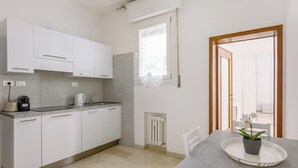 Een moderne keuken met witte kasten, een inbouwoven en een eethoek met een tafel en stoelen.
