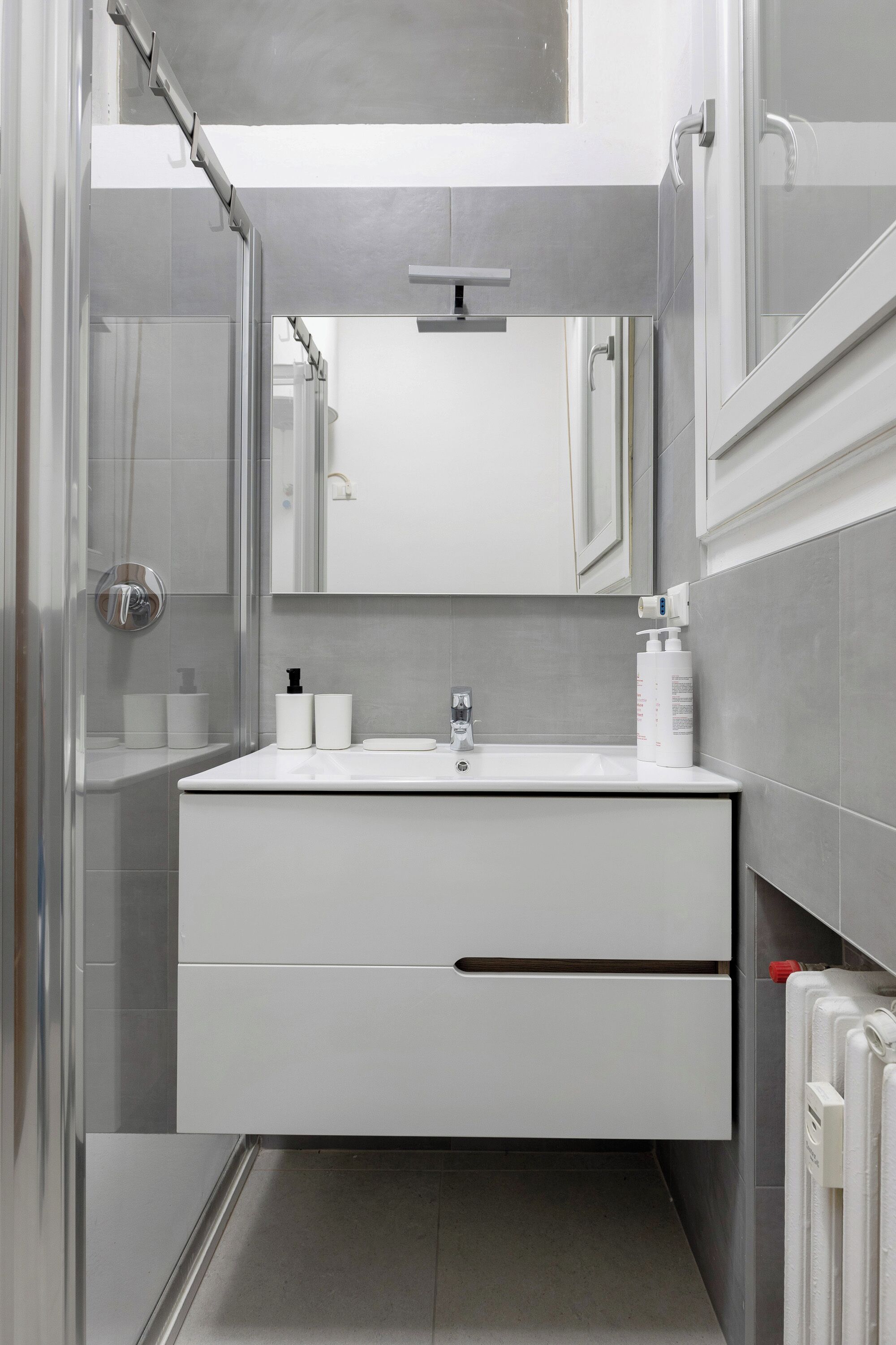 Un baño moderno con un tocador blanco, un espejo y una zona de ducha.