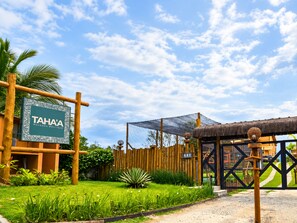 Skilt for TAHAA Pousada Boutique, et træhegn, en stråtækt bygning og et græsstykke med beplantning.