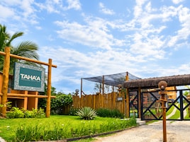 Señal de TAHAA Pousada Boutique, cerca de una valla de madera, una estructura con techo de paja y un área verde con plantas.