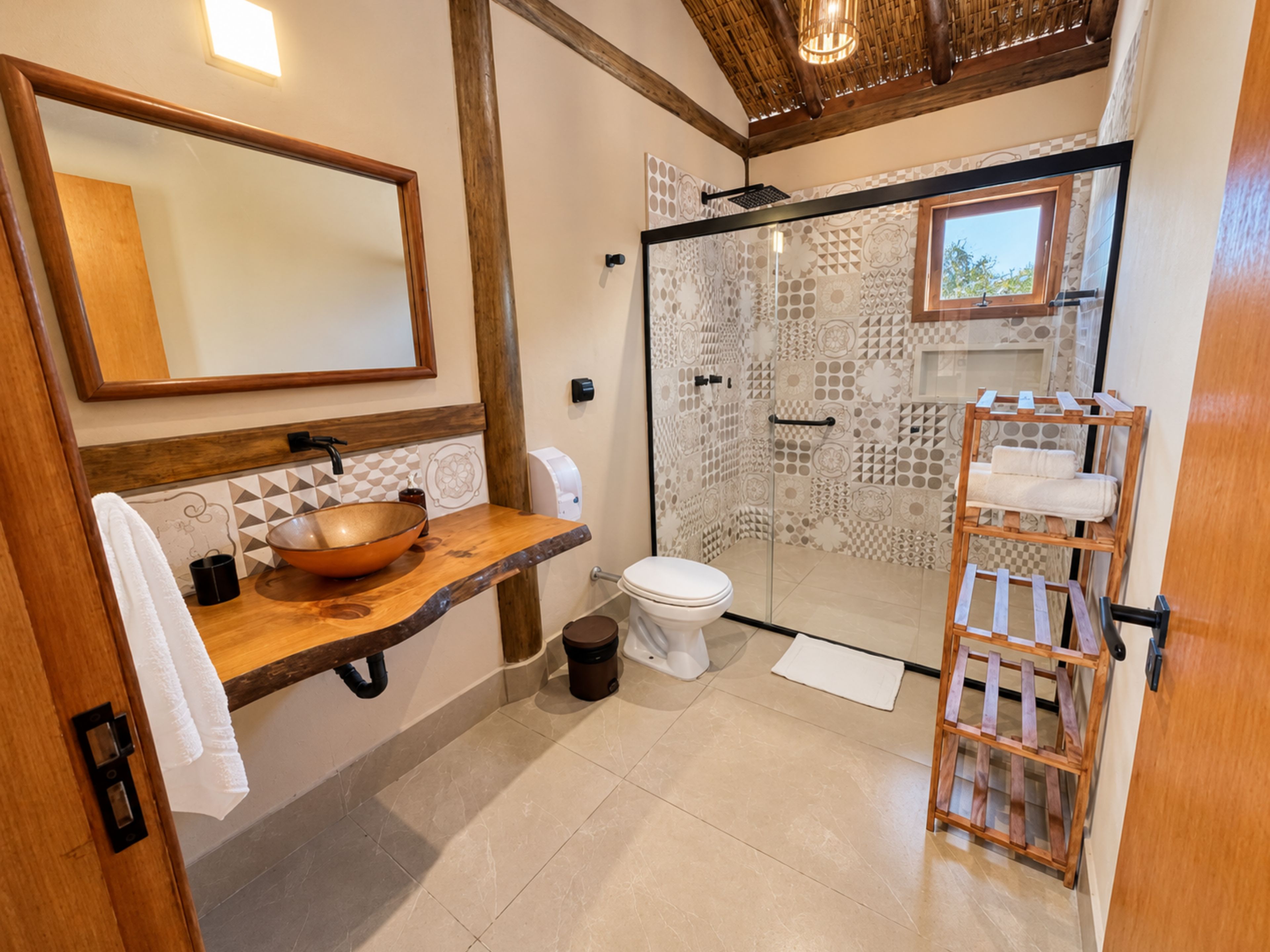 A bathroom with a wooden vanity, a large mirror, a glass shower enclosure, and a wooden towel rack.